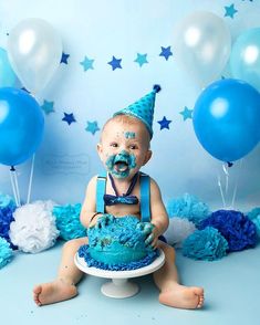 a baby sitting in front of a cake with blue frosting and balloons around it