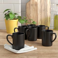 four black coffee mugs sitting on top of a wooden table next to a potted plant