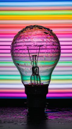 a light bulb sitting on top of a table in front of a rainbow colored wall