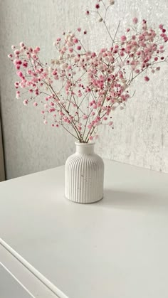 a white vase filled with pink flowers sitting on top of a white dresser next to a wall