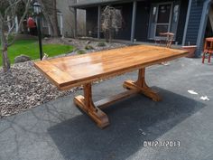 a wooden table sitting in the middle of a driveway next to a house with chairs