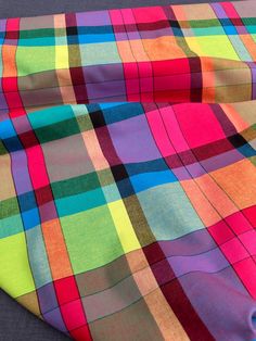 a multicolored plaid fabric is laying on top of a gray surface with a blue hole in the middle