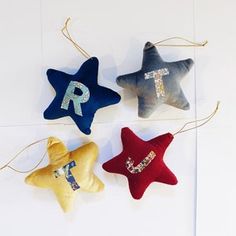 three star shaped ornaments hanging from strings on a white wall, one with the letter r in sequins