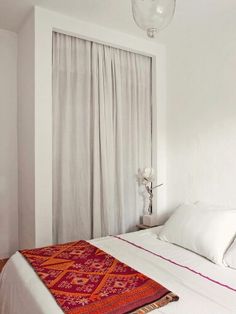 a bed with white sheets, pillows and a red blanket on top of it next to a window