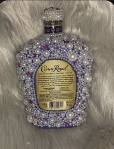 a bottle with pearls on it sitting on a white fur covered surface, in the shape of a crown