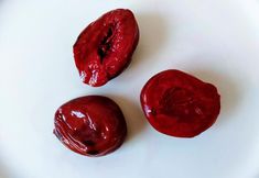 three pieces of red fruit sitting on top of a white plate next to each other