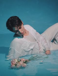 a woman laying on the ground with flowers in her lap and wearing white clothes, next to a pool