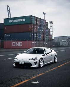 a white sports car parked on the side of an empty road in front of shipping containers