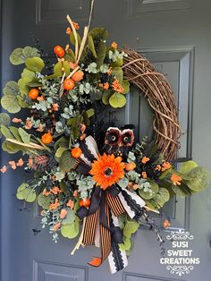 a wreath with orange flowers and leaves hanging on the front door to give it an autumn feel