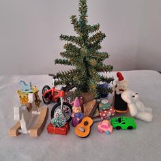 a small christmas tree surrounded by toys and other items on a bed with white sheets