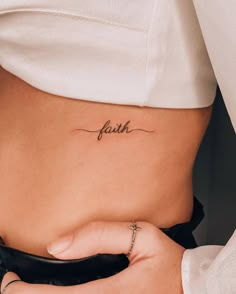 a woman's stomach with the word faith tattooed on her lower side ribcage