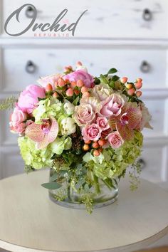 a vase filled with pink and green flowers on top of a table next to a dresser