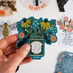 a hand holding a sticker with flowers in a jar surrounded by other stickers