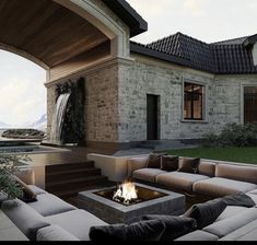 a living room with couches and a fire pit in front of a stone house