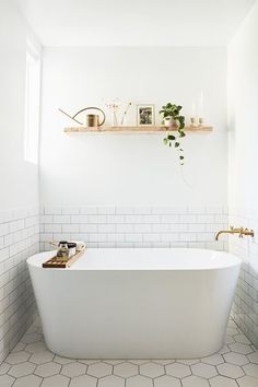 a white bath tub sitting under a window next to a shelf filled with plants and candles