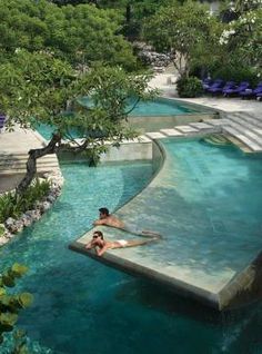 two people are laying on the edge of an artificial swimming pool in a tropical setting