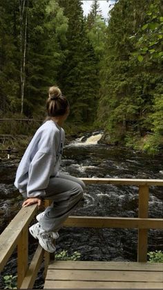 a woman is sitting on a wooden bridge over a river and looking at the water