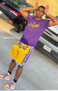 a man in purple shirt and yellow shorts holding his hands up to his head while standing next to a car