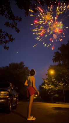 a woman standing in front of a firework display with her back to the camera