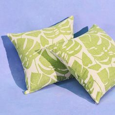 two green and white pillows sitting on top of a blue surface with the same pattern