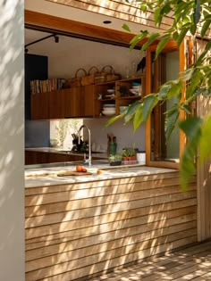 an outdoor kitchen with wooden cabinets and counter tops is seen through the shade of a leafy tree