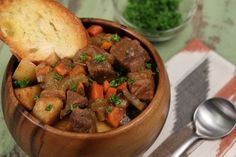 a wooden bowl filled with meat and vegetables next to a piece of bread on top of a table