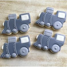 four decorated cookies in the shape of cars on a wooden table with white frosting