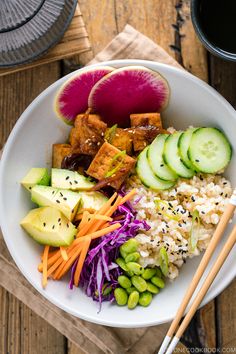 a bowl filled with rice, cucumber, carrots and other vegetables next to chopsticks