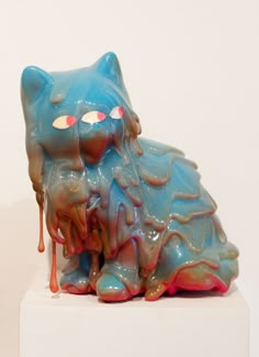 a blue and red cat statue sitting on top of a white pedestal next to a wall