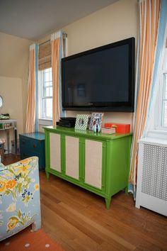 a flat screen tv sitting on top of a green cabinet in a living room next to a window