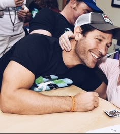 two men sitting at a table and one is holding his arm around the other man's shoulder