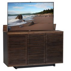 a flat screen tv sitting on top of a wooden cabinet next to the ocean and rocks