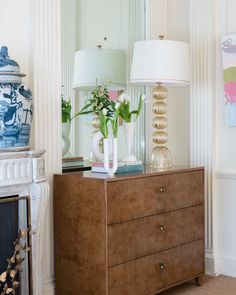 a dresser with two vases and flowers on it in front of a fire place