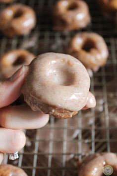 a person holding a doughnut in front of several other donuts on a rack