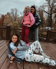 three women posing on a wooden deck with trees in the background and one woman laying on the ground