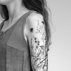 a woman wearing a sleeve tattoo with flowers on her left arm and a bee sitting on the flower