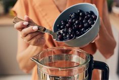 a woman is holding a spoon over a blender filled with blueberries