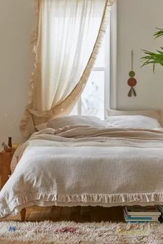 a white bed sitting under a window next to a wooden table with a potted plant on top of it