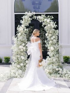 a woman standing in front of a white arch with flowers