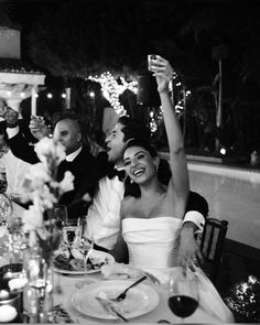 a bride and groom sitting at a table with their arms in the air as they toast