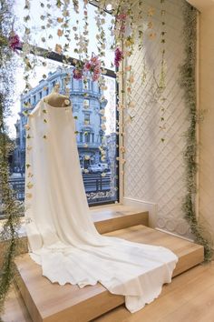 a white dress on display in a window with flowers hanging from the windowsills