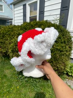 a hand is holding up a white teddy bear wearing a red and white santa hat