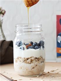 a jar filled with oatmeal and blueberries being drizzled over it