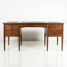 a wooden desk with two drawers sitting on top of white floored room next to wall