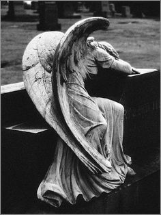 an angel statue sitting on top of a bench next to a grass covered park area