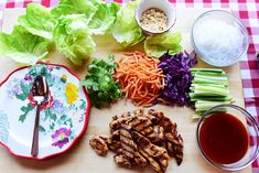 a cutting board topped with lettuce, carrots and other vegetables next to dipping sauce