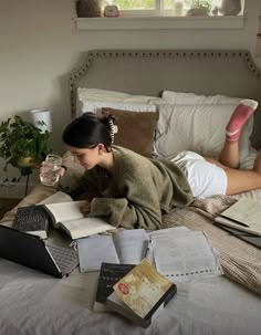 a woman laying in bed with books and laptops