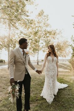 a bride and groom hold hands as they walk through the grass