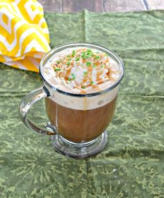 hot chocolate with whipped cream and sprinkles in a glass mug on a green tablecloth