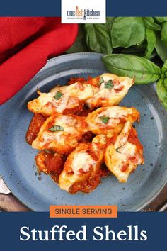 a blue plate topped with stuffed shells covered in cheese and sauce next to spinach leaves